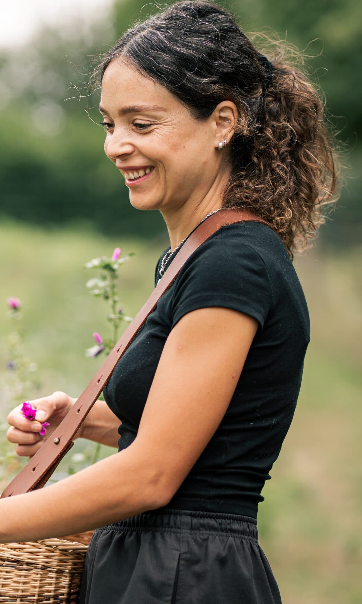 Alexandra Chennevière cueille des fleurs de mauve, panier en osier à l'épaule